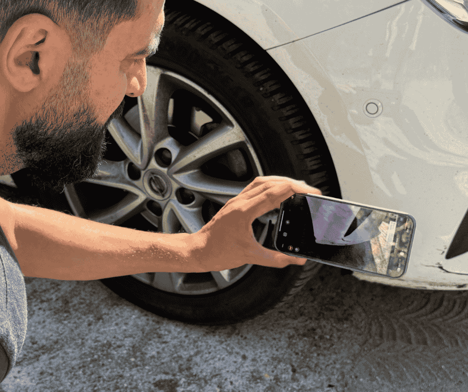 Ein Mann nutzt sein Smartphone für den Live Video Support, um einen Schaden an seinem weißen Auto zu dokumentieren.