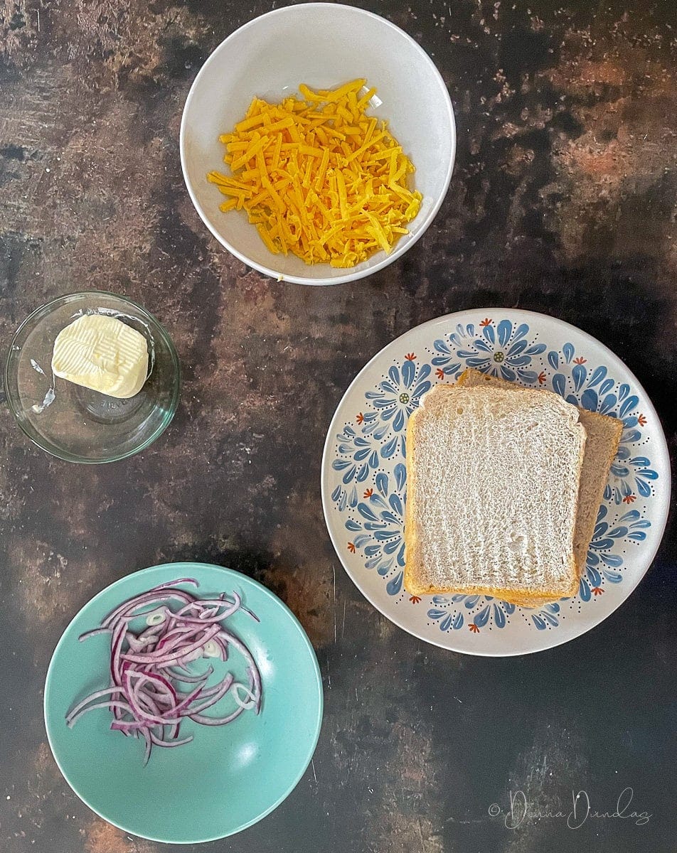 bread, sliced onions, grated cheese and butter on table in bowls.
