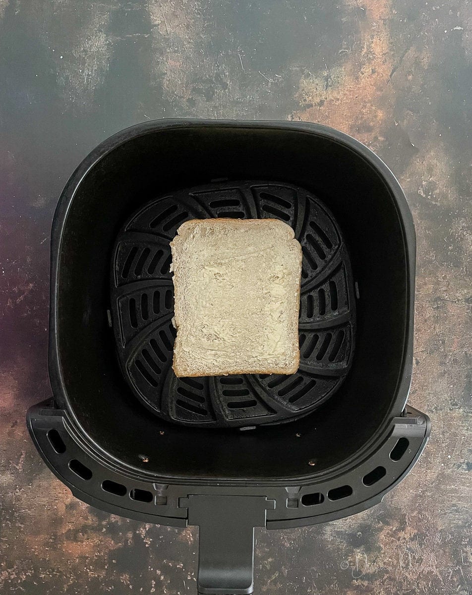 bread spread with butter in air fryer basket.