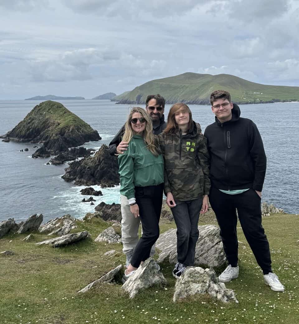 Family enjoying scenic coastal view with rocky cliffs and lush green hills in the background.