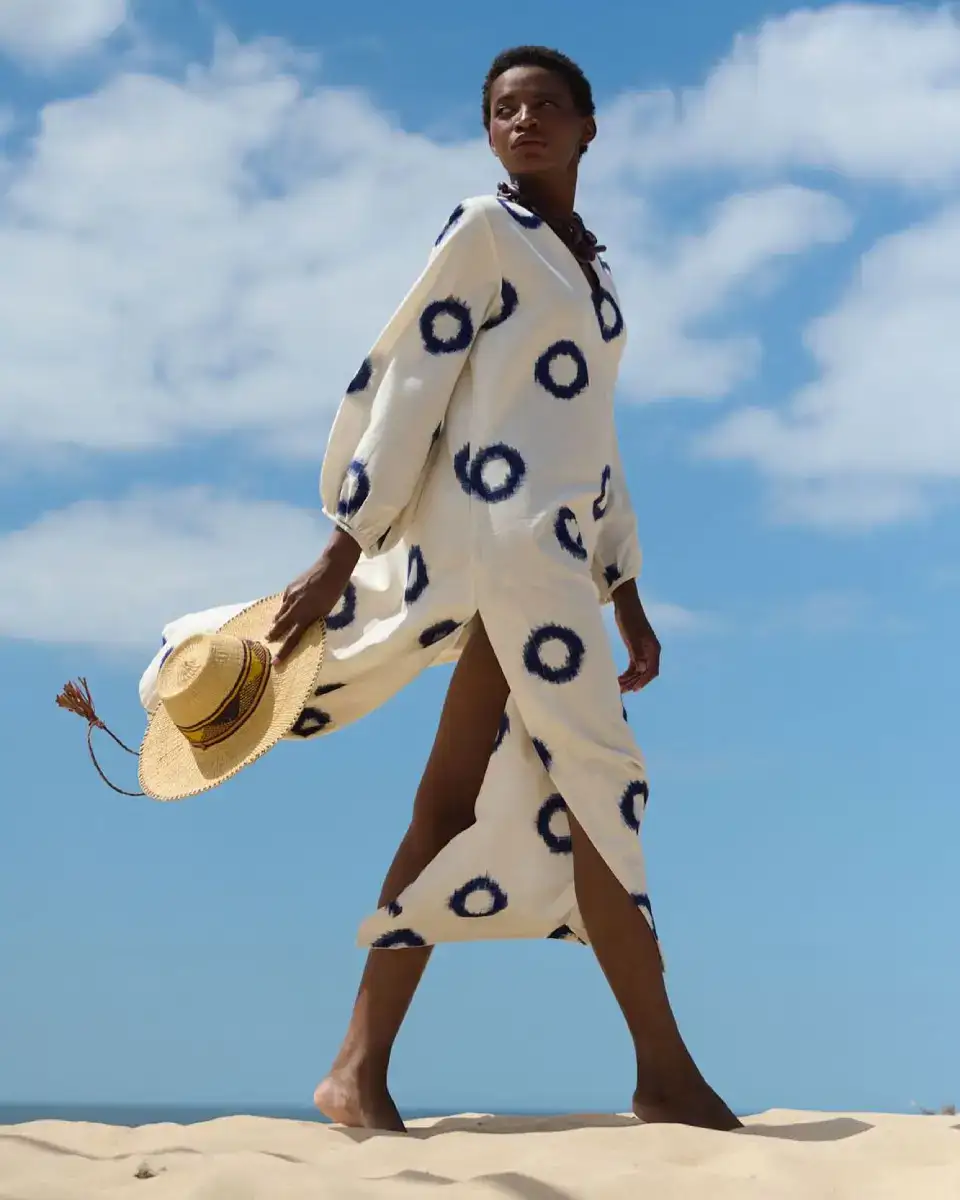 Modelo con vestido artesanal blanco y azul de KLEED sobre dunas. Luxury travelwear y resortwear contemporáneo representado en España.