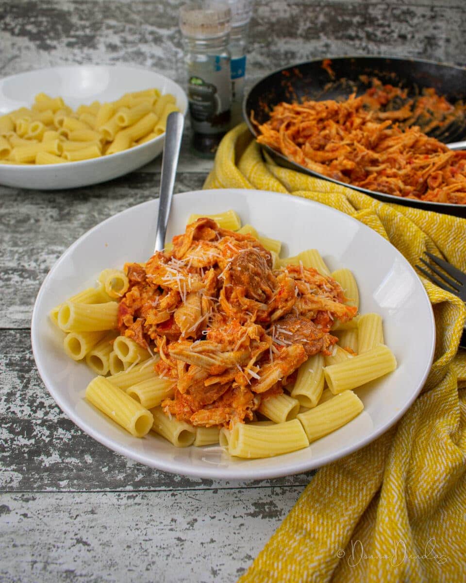 Served bowl of leftover roast chicken pasta in white pasta bowl. Frying pan, bowl of pasta and salad bowl to the sides.