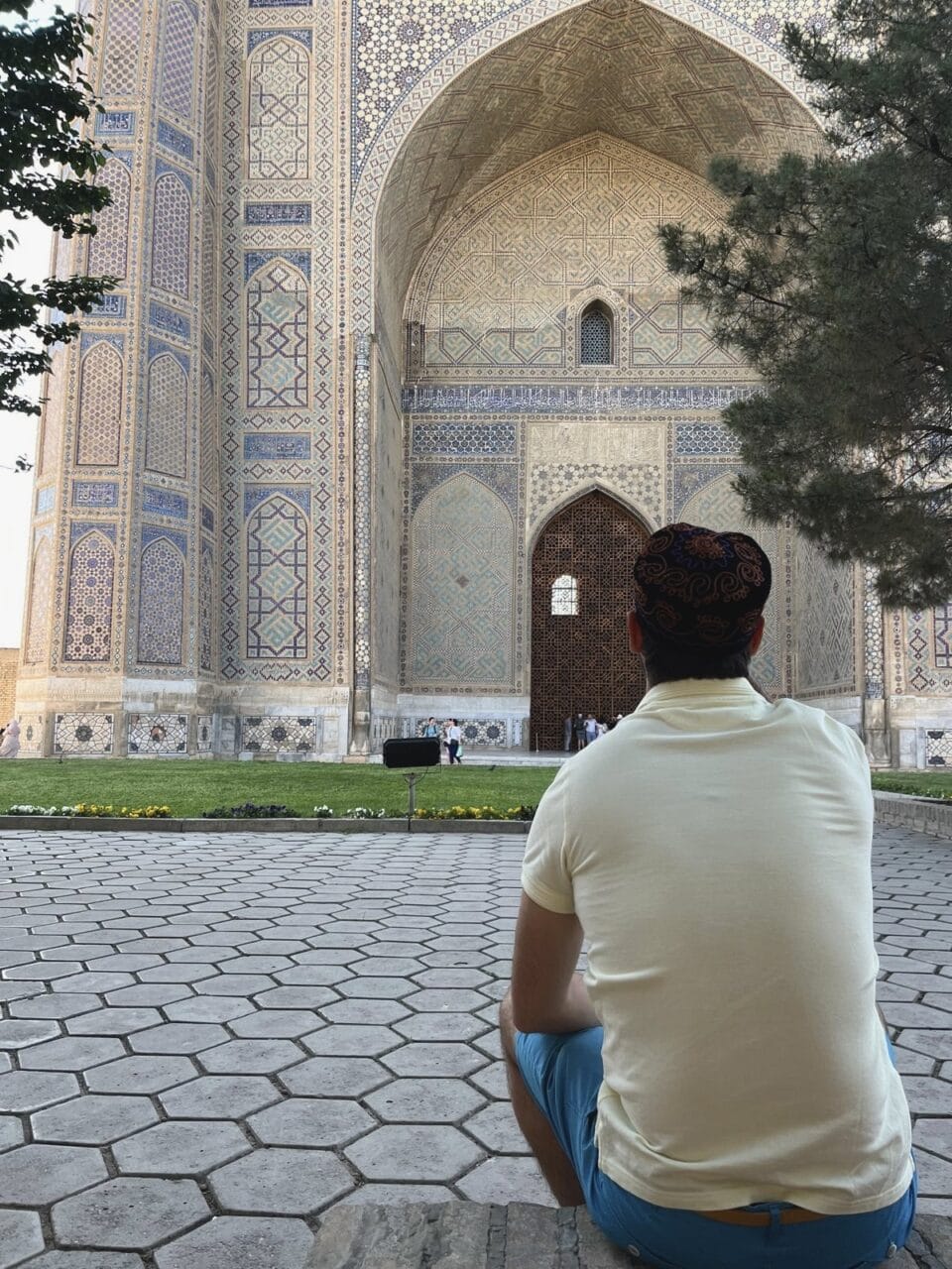 Man in yellow t-shirt sitting in front of a massive and ornate ancient gate in samarkand