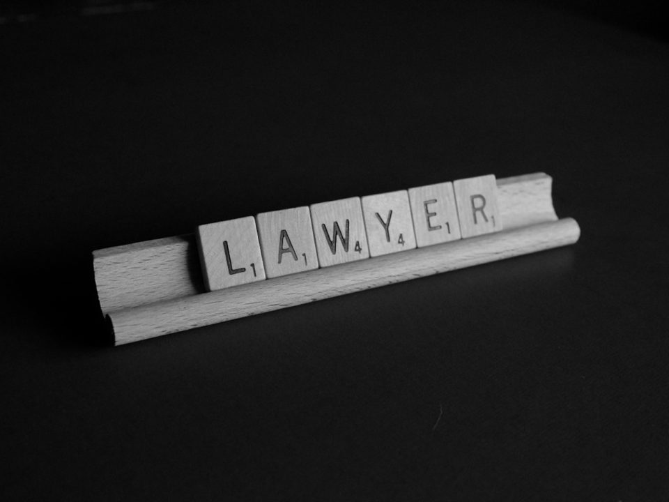 Scrabble tiles on a rack spelling out the word "LAWYER" against a black background.