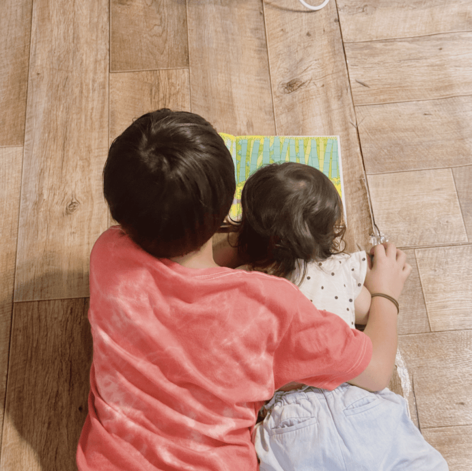 兄と妹が床に寝転んで絵本を読んでいる