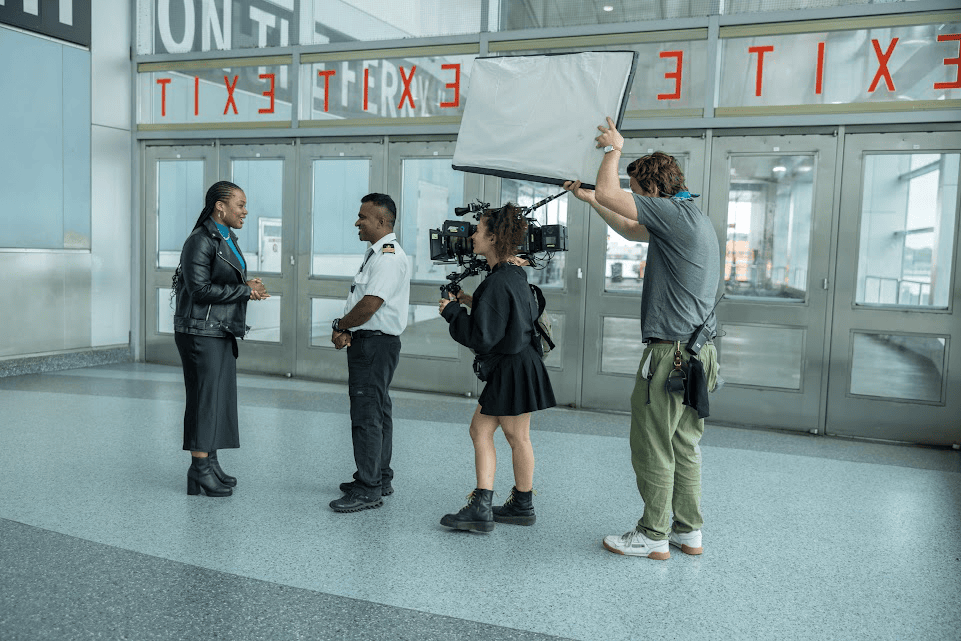 An image of a woman interviewing a company guard while being filmed