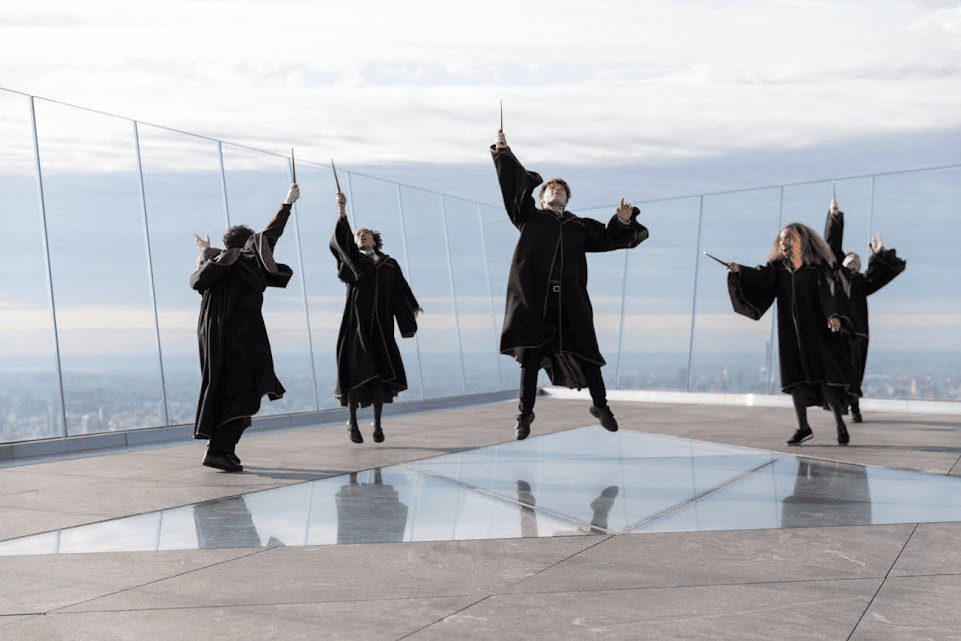 An image of some kids jumping in the air with wands in their hands while wearing gowns