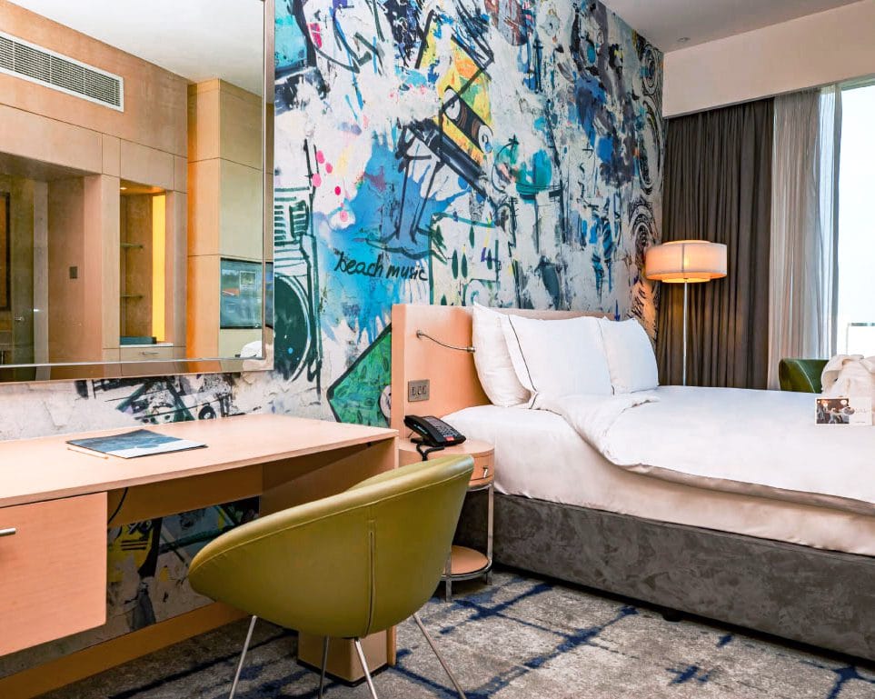 coolroom_1-min-1 Stylish hotel room with an artistic graffiti wall, modern desk setup, and a cozy king-size bed.