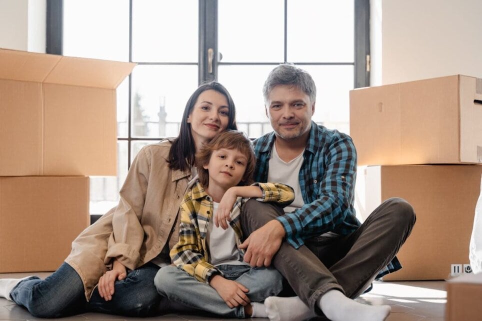 A Family Sitting in the Floor with Moving Boxes on the Background
