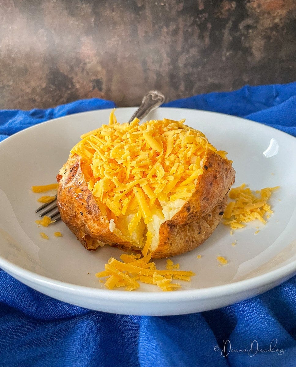 Close up side view of baked potato with grated cheese piled on top.
