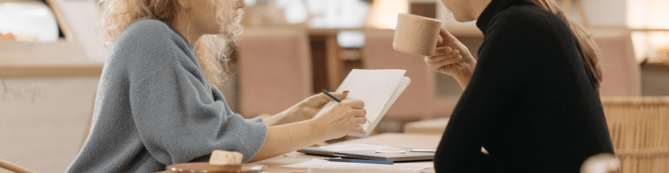 Image of two staff talking while one takes notes.