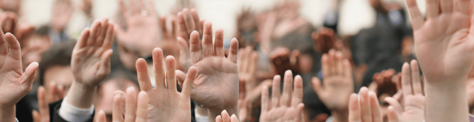 Image of a room full of employees holding their hands up to vote.