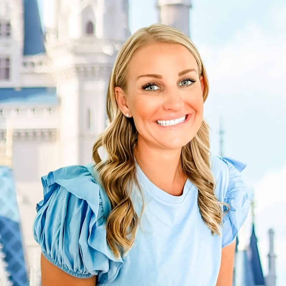 Smiling woman in blue dress with castle background, promoting 407 and Beyond Vacation Co.