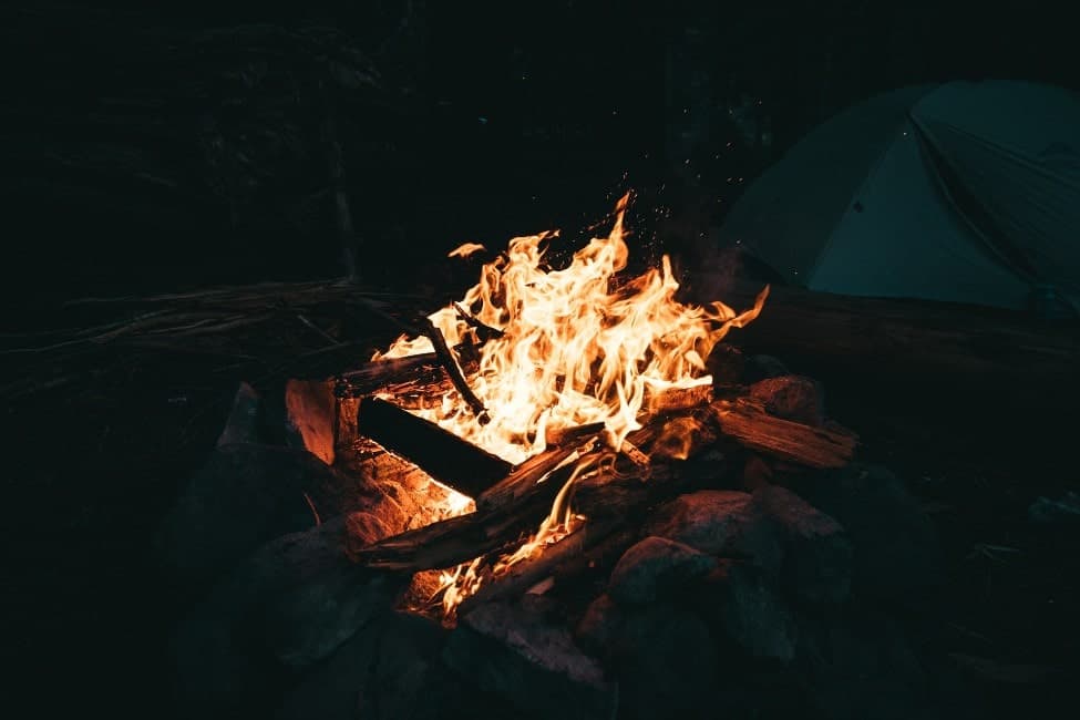 photo of a campfire with a tent in the background