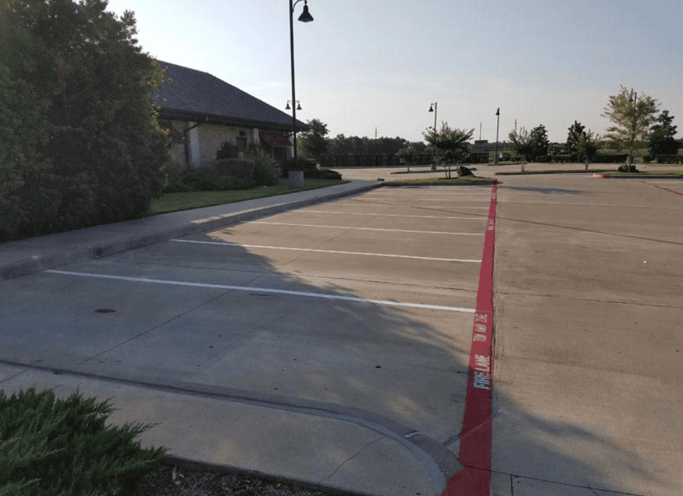 Concrete parking lot with freshly painted white stall lines and a bright red fire lane curb with stenciled FIRE LANE TOW AWAY ZONE lettering