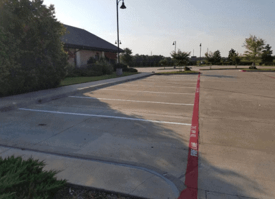 Concrete parking lot with freshly painted white stall lines and a bright red fire lane curb with stenciled FIRE LANE TOW AWAY ZONE lettering