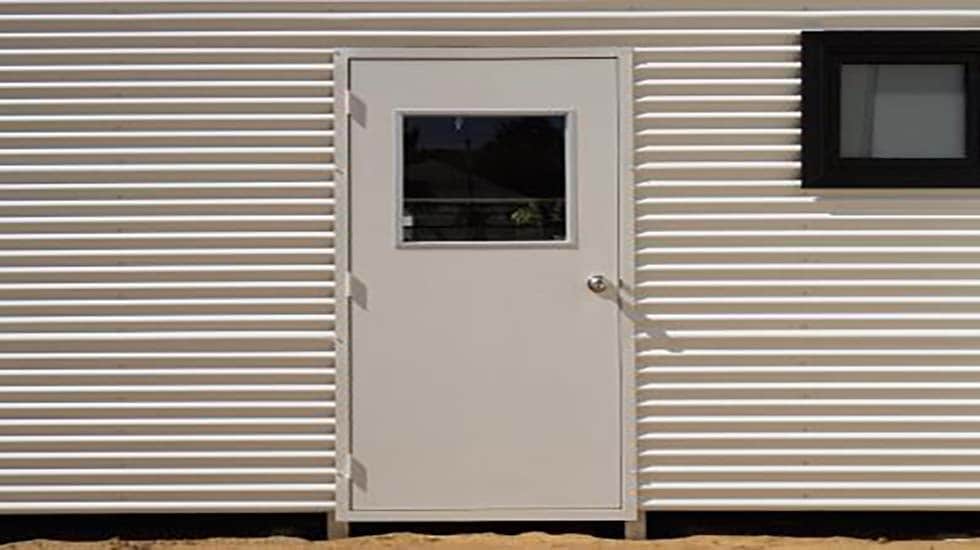 White personal access door with a window, installed in a corrugated metal building