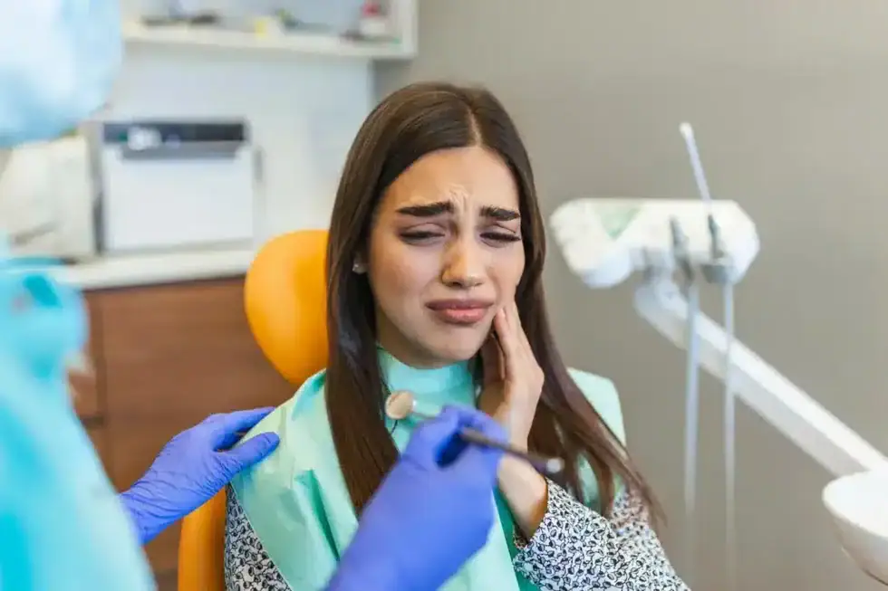 Patient holding cheek with pain during dental visit for root canal treatments in Riverview, MI