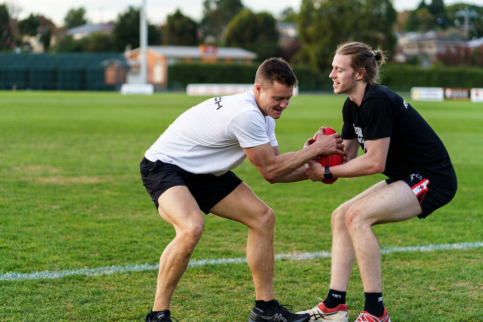 Two athletes engaged in a one-on-one football training drill on a grassy field.