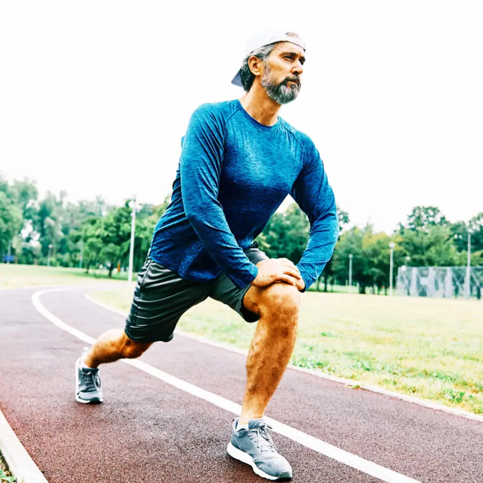 Man stretching on a running track before a workout, representing enhanced muscle recovery, energy, and cellular health from NAD+ Therapy at BionwoRx in Carmel, Indiana.