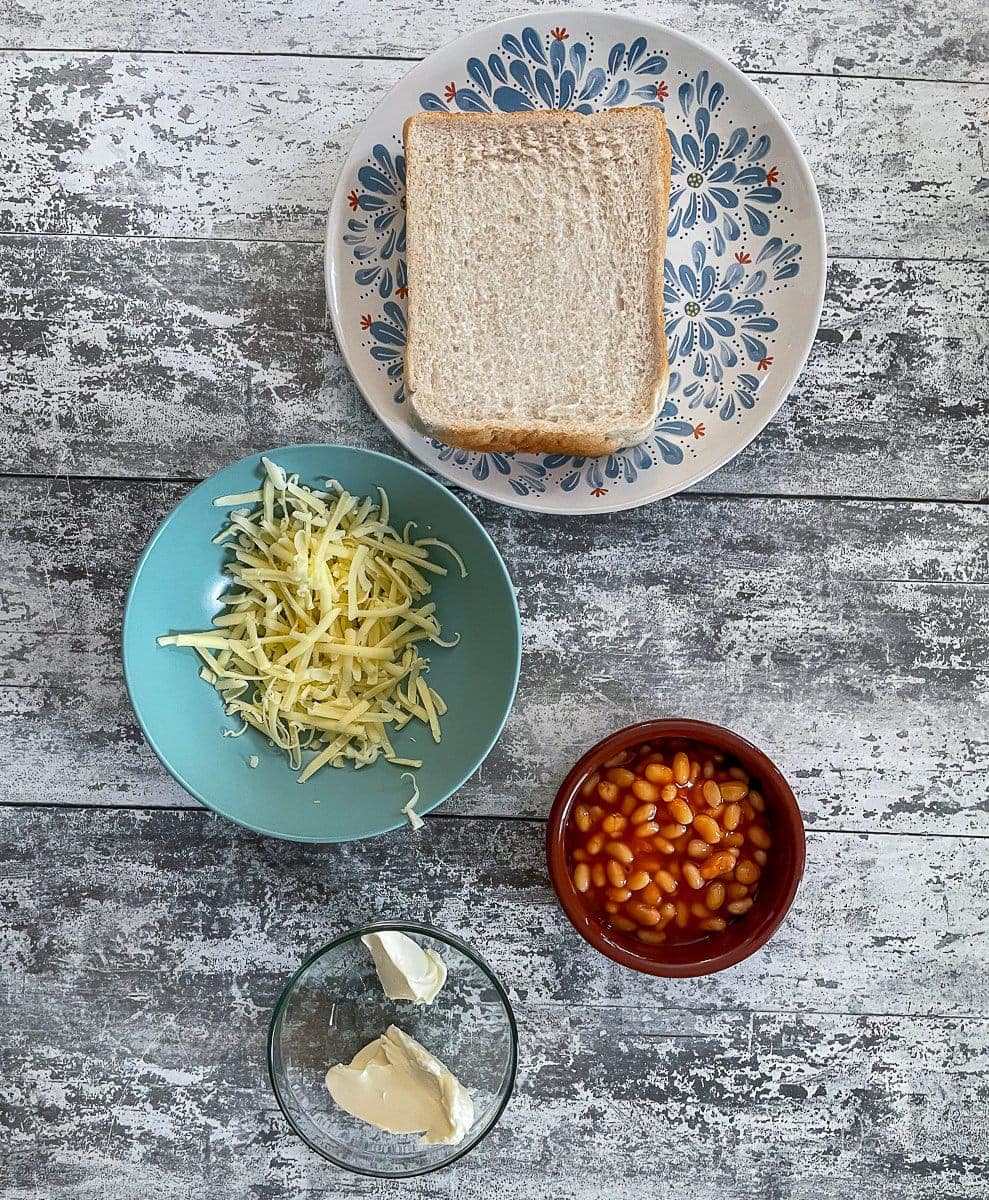 bread, greated cheese, baked beans and butter on table.