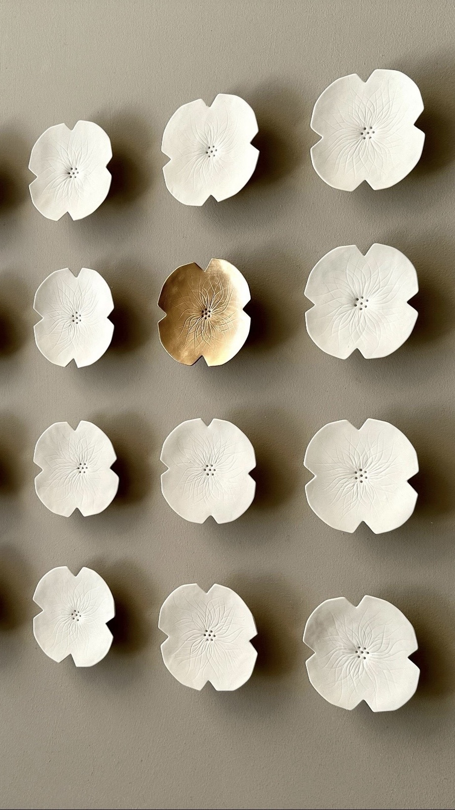 Layered porcelain rosette wall flowers casting soft shadows, sculptural wall art for interior design.
