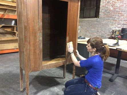 Theresa Clement with the restored cabinet. It, along with other ReStore-made pieces, will be offered at auction at the store from Jan. 25 to Feb. 1.