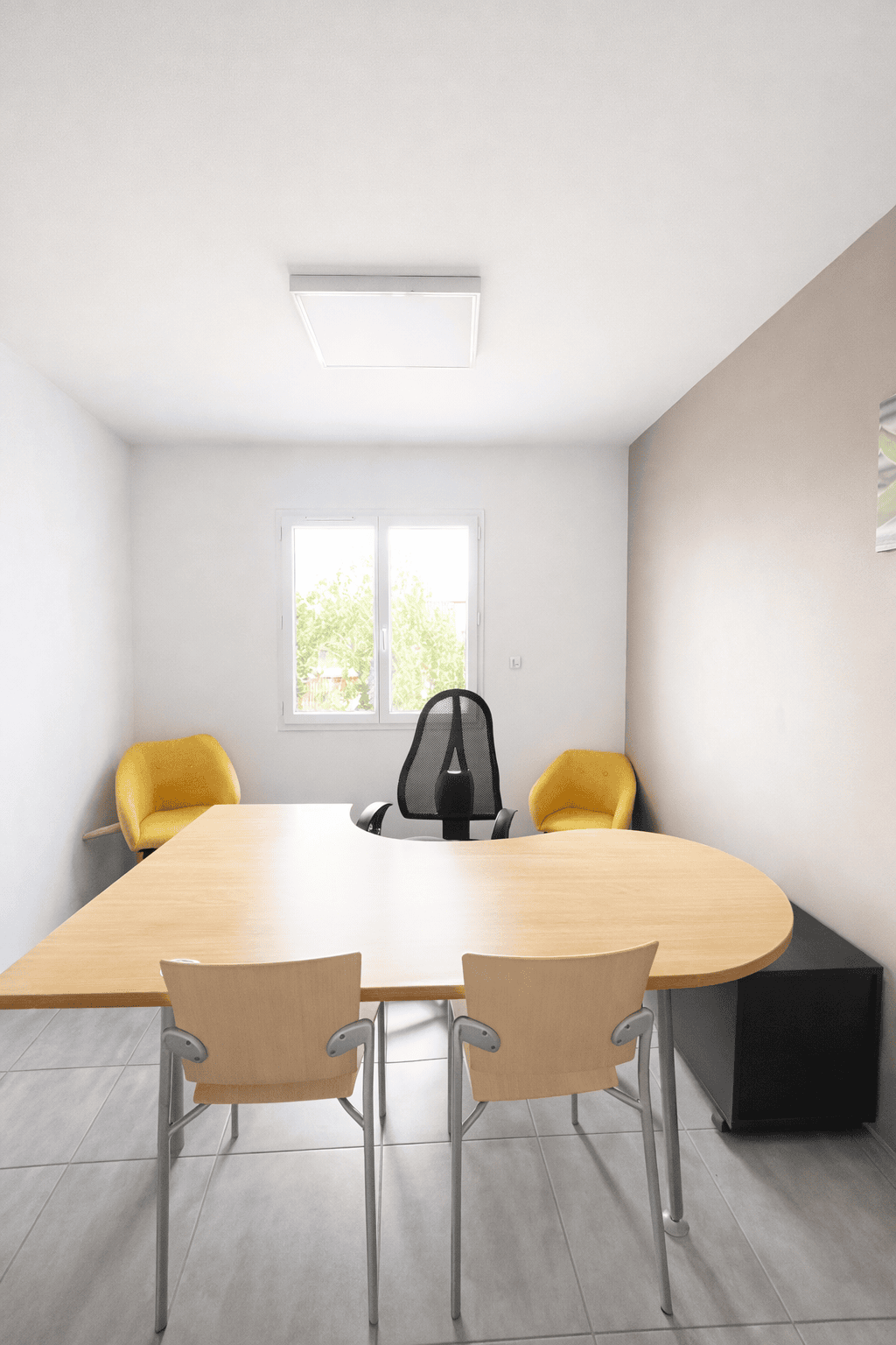 Bureau à louer moderne et lumineux avec table ergonomique en bois clair et deux fauteuils jaunes.