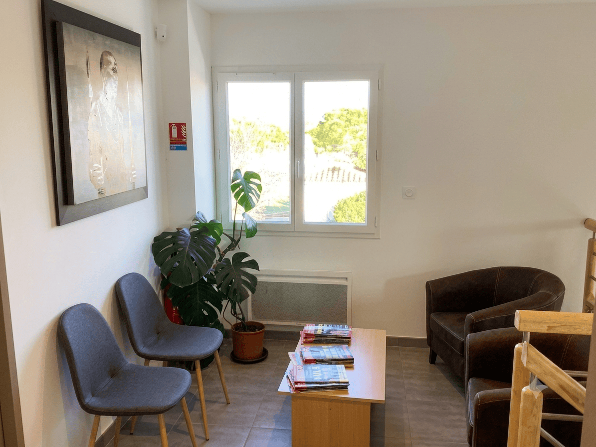 Espace d'attente pour clients avec table basse, magazines et porte d'accès aux sanitaires WC.