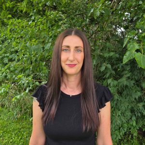 Julie Stewart outdoors with lush green foliage background for vacation planning.