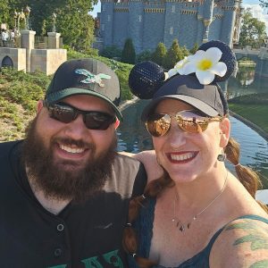 Happy couple at Disney castle with Mickey Mouse ears and flower accessory.