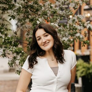 Happy woman standing outdoors near blooming trees and brick buildings.