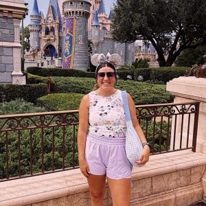 Enchanting Disney castle with a smiling woman in front, experiencing a magical vacation at Disneyland.