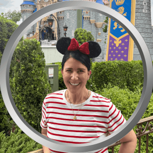 Smiling woman with Minnie Mouse ears at Disney theme park with castle backdrop.