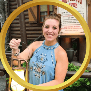 407 Vacation Co. woman holding lantern at an outdoor restaurant with a rustic log cabin background.