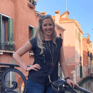 Smiling woman standing by Venice canal with colorful buildings.