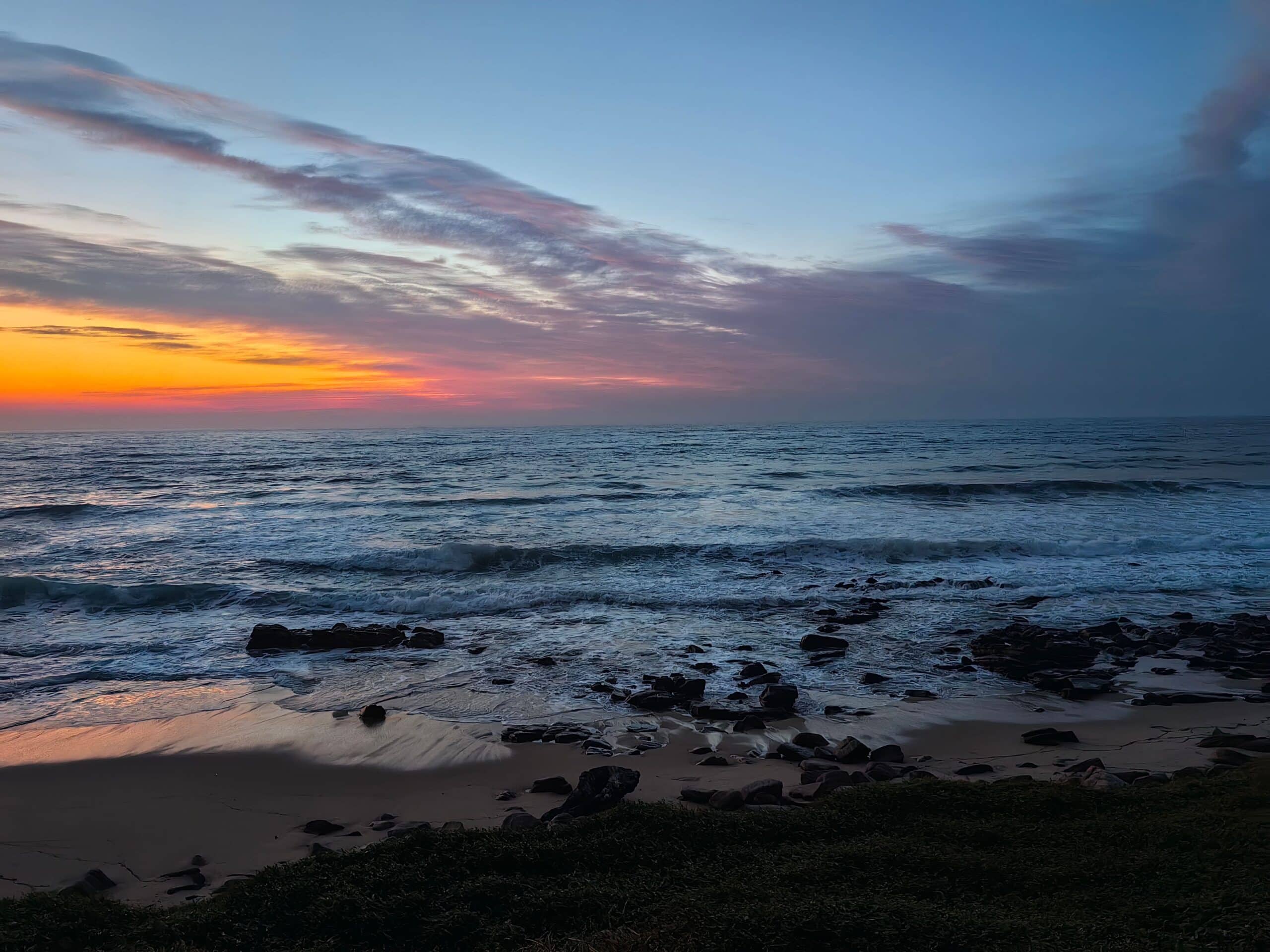 Peaceful ocean sunrise with colorful sky and rocky beach. Ideal for travel and nature themes.