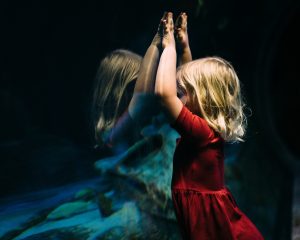 Little Girl Pressing Hands Against Aquarium Glass Reflection