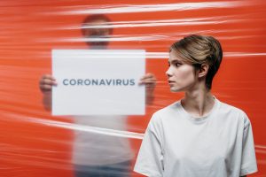 Woman Looking Back Near A Person Holding A Coronavirus Sign Behind Plastic Wrap
