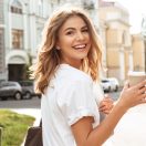 Portrait of smiling european woman strolling through city street with silver laptop and takeaway coffee in hands