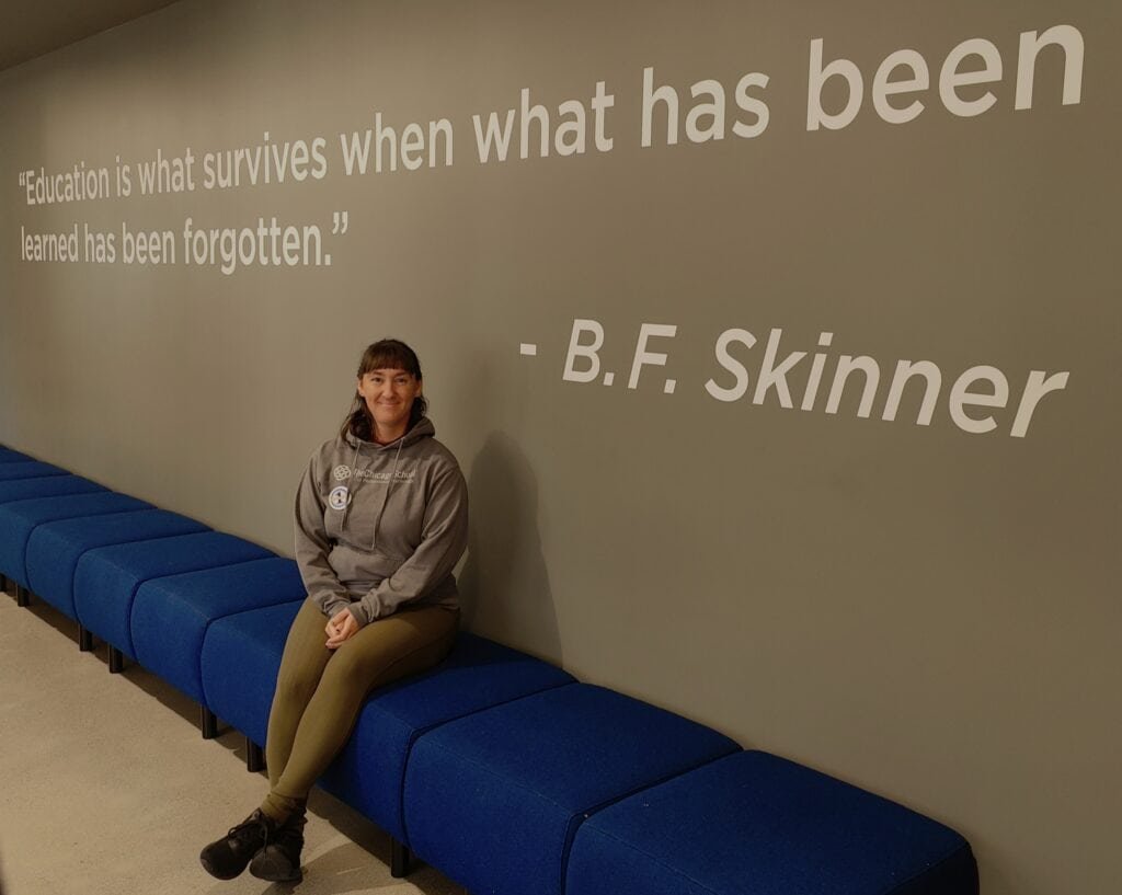CEO seated on blue chairs with a quote from BF Skinner written on the wall behind. The quote says, "Education is what survives when what has been learned has been forgotten." 