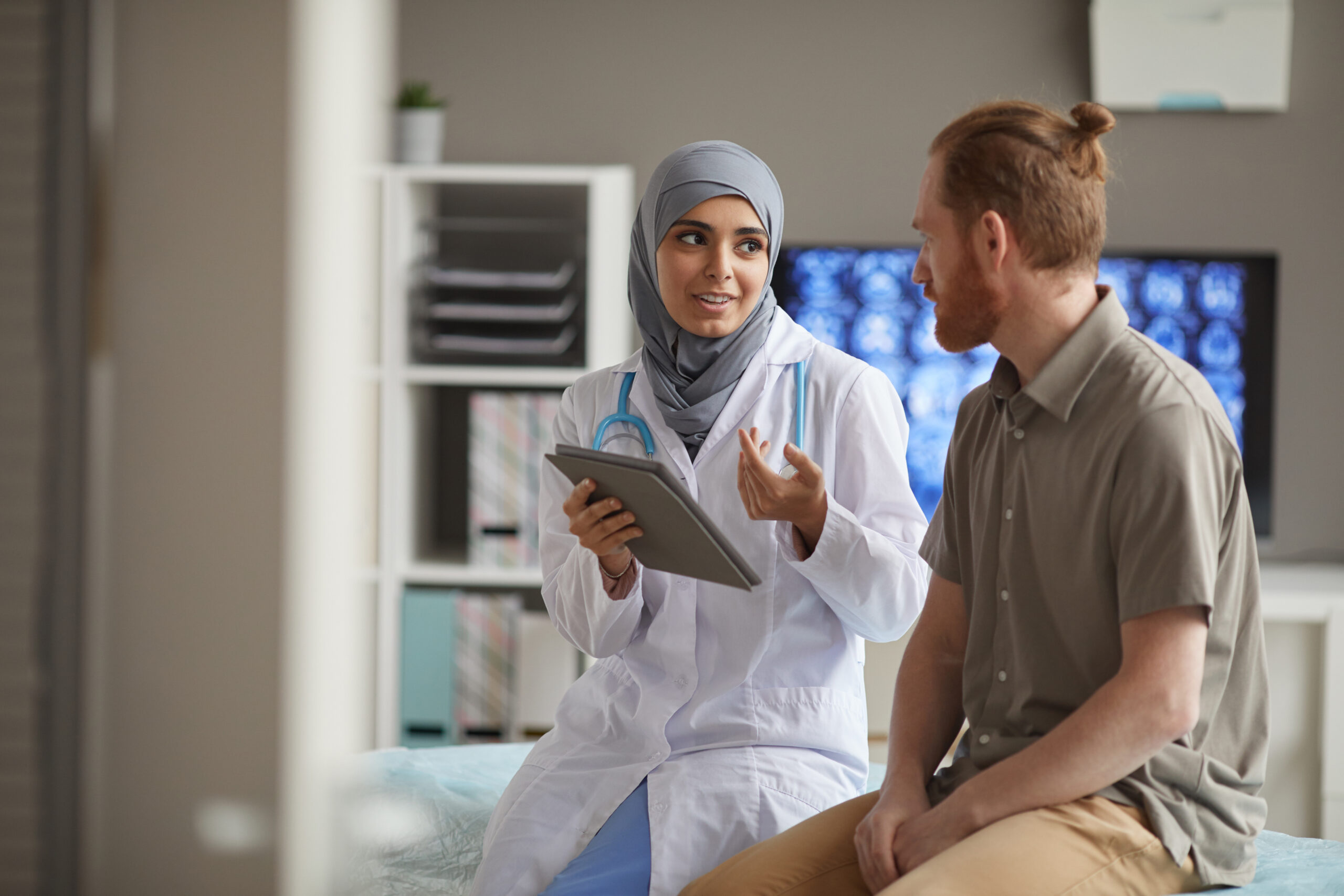 Female doctor consulting male patient with digital tablet in modern medical office.