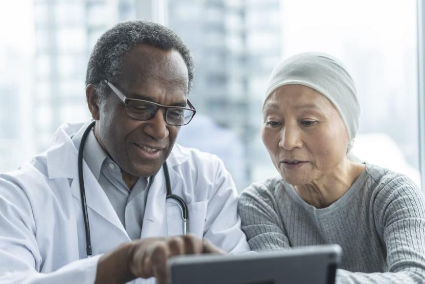 Doctor consulting with cancer patient using tablet for personalized treatment plan in modern healthcare setting.