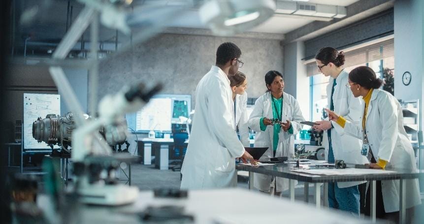 Team of scientists collaborating in modern lab environment with lab coats, microscopes, and advanced equipment.