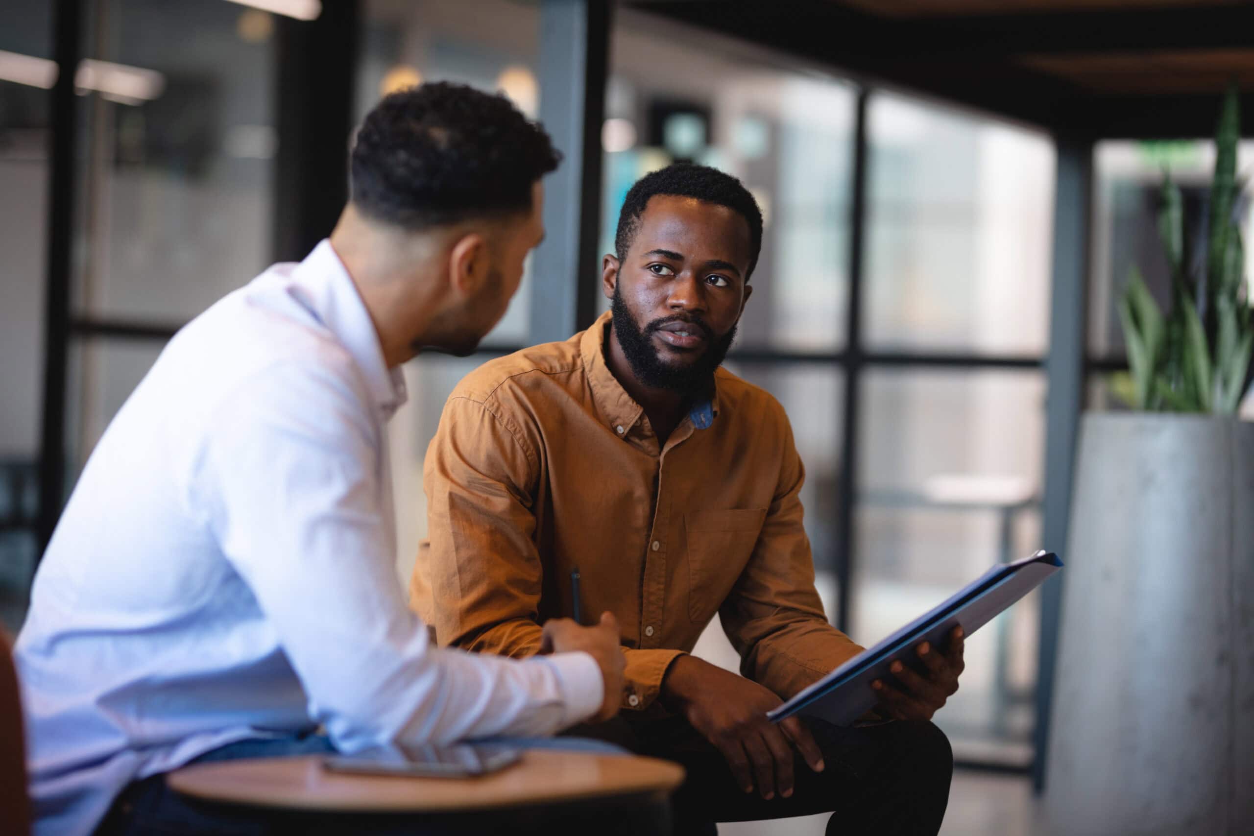 Two professionals having a serious business discussion in modern office setting with documents and laptops.