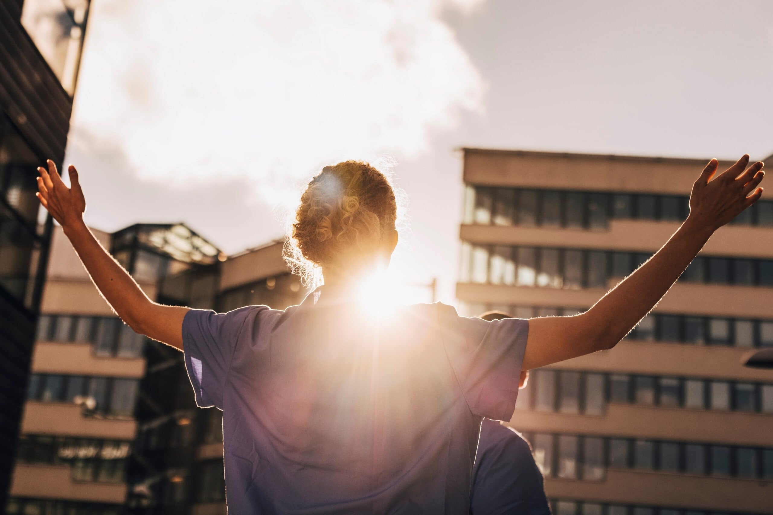 Healthcare worker raising arms in sunlight outside hospital