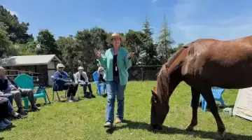 Woman presenting to a seated group outdoors with a horse nearby during a PMR educational workshop