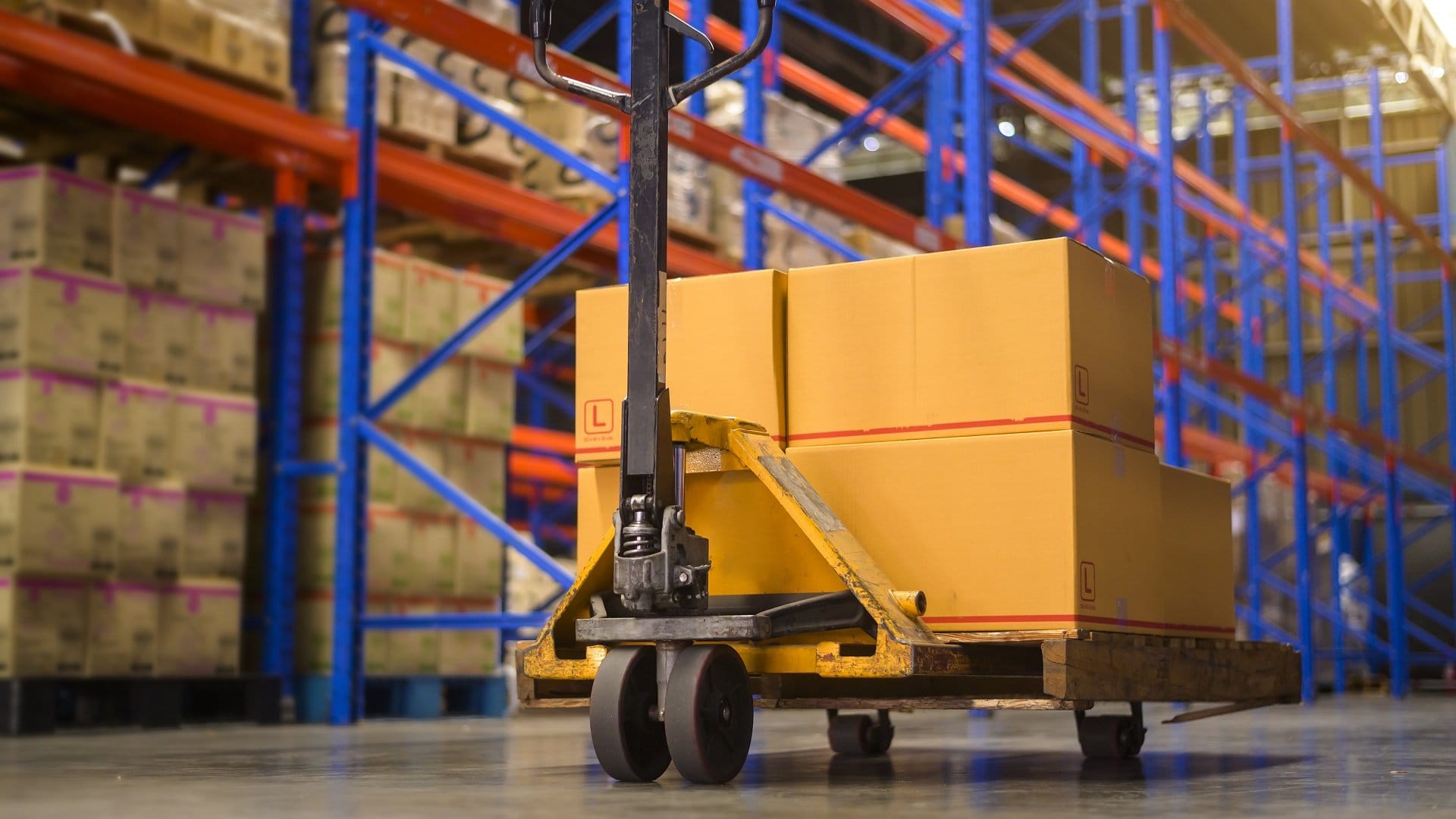 A pallet jack loaded with boxes beside a shelf