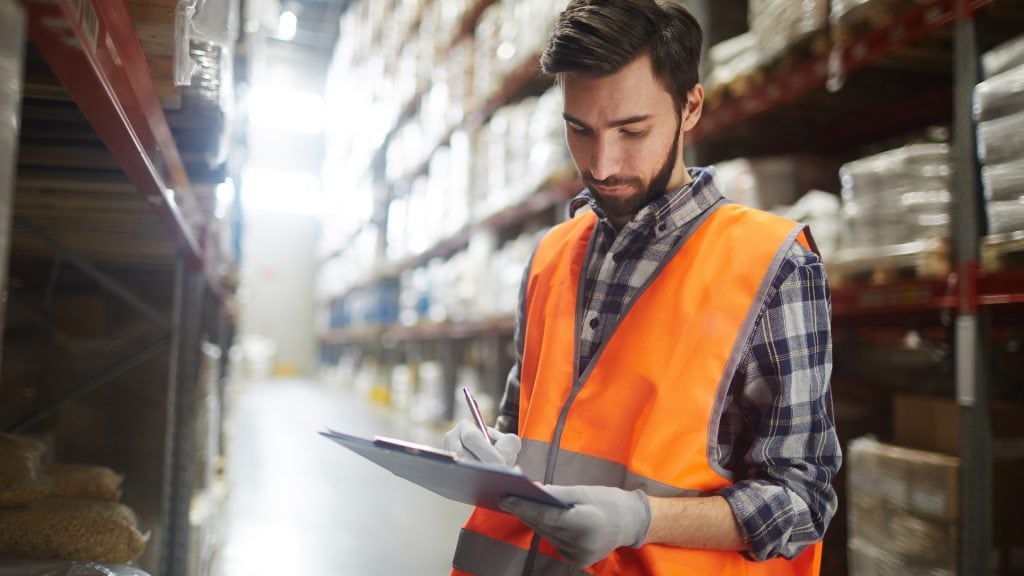 Worker in warehouse with orange vest and clipboard