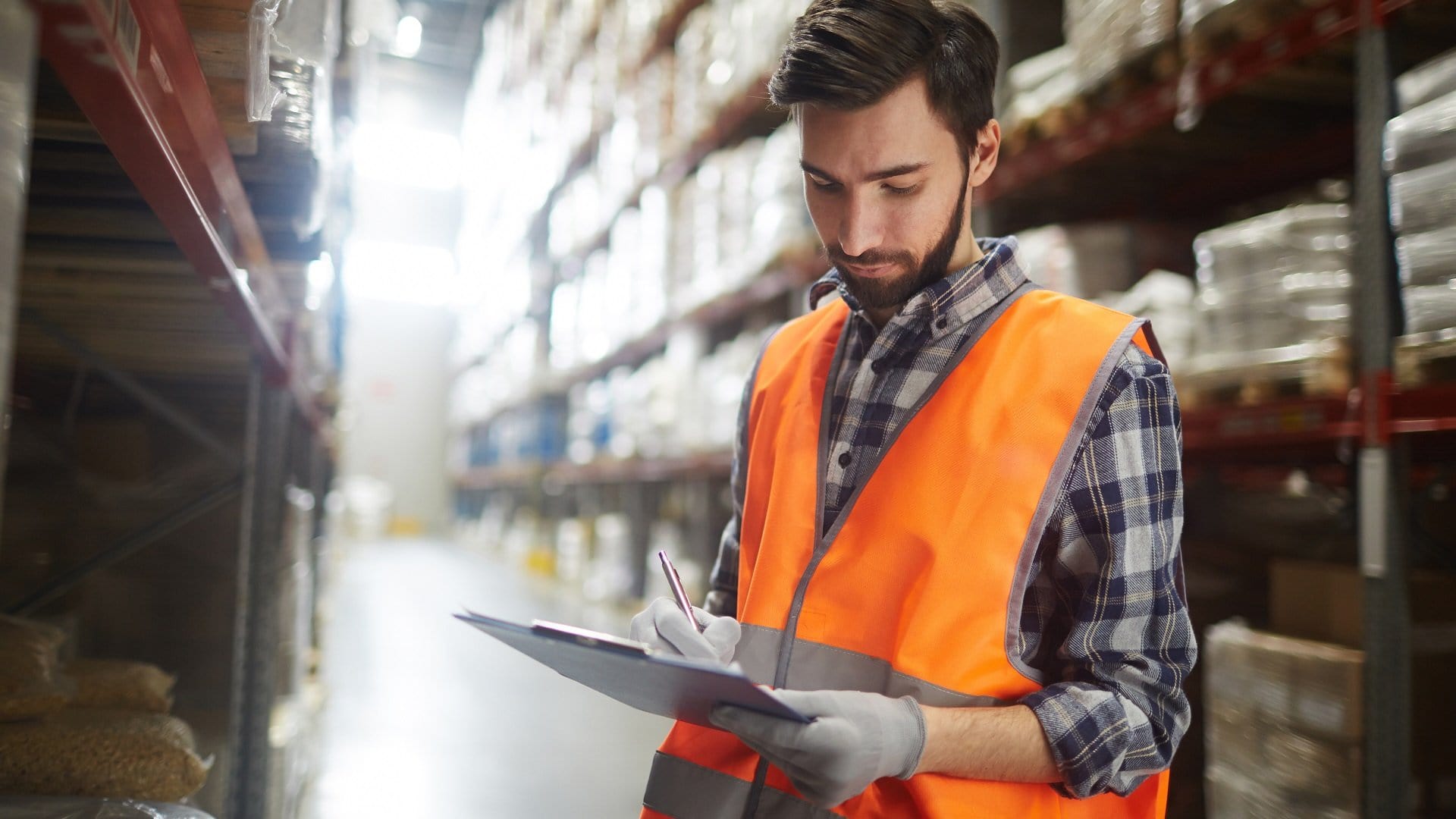Worker in warehouse with orange vest and clipboard